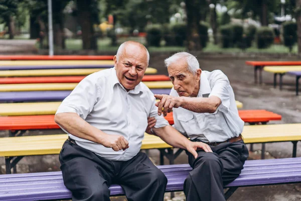 Two old senior adult men have a conversation outdoors in the city park