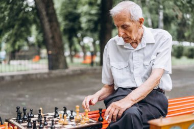 Parktaki bankta satranç oynayan iki yetişkin adam.