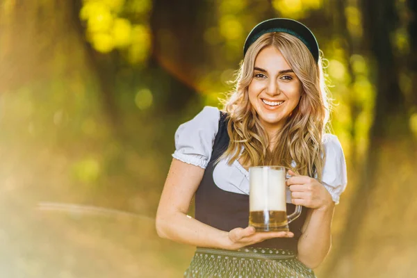 汚れでかなり幸せなブロンド 伝統的な祭りのドレス ぼやけた背景を持つフィールドに屋外ビールの2つのマグカップを保持 オクトーバーフェスト 聖パトリックの日 国際的なビールの日のコンセプト — ストック写真