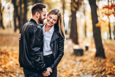 Genç bir çiftin portresi. Kadın ve erkek, sonbahar parkının arka planında sarılıp gülümsüyor..
