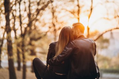 Romantik bir çift bankta oturup parkta gün batımını seyrediyor. Aşk hikayesi. Arka plan.