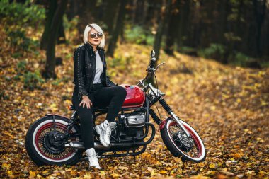 Kırmızı motosikletli, güneş gözlüklü güzel sarışın motosikletli kız. Ormanda yol kenarında. Renkli, bulanık bir geçmişi var..
