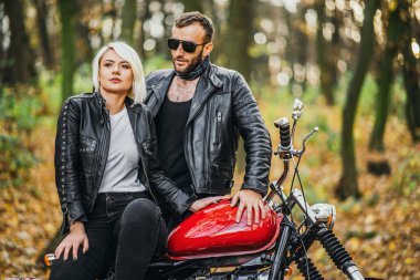 Ormandaki yolda, kırmızı motorsikletin yanında, renkli, mavi arka planda güzel bir çift. İlişki kavramı.