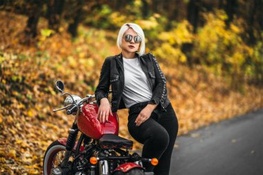 Kırmızı motosikletli, güneş gözlüklü güzel sarışın motosikletli kız. Ormanda yol kenarında. Renkli, bulanık bir geçmişi var..
