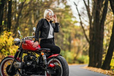 Kırmızı motosikletli, güneş gözlüklü güzel sarışın motosikletli kız. Ormanda yol kenarında. Renkli, bulanık bir geçmişi var..