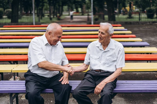 Two old senior adult men have a conversation outdoors in the city park