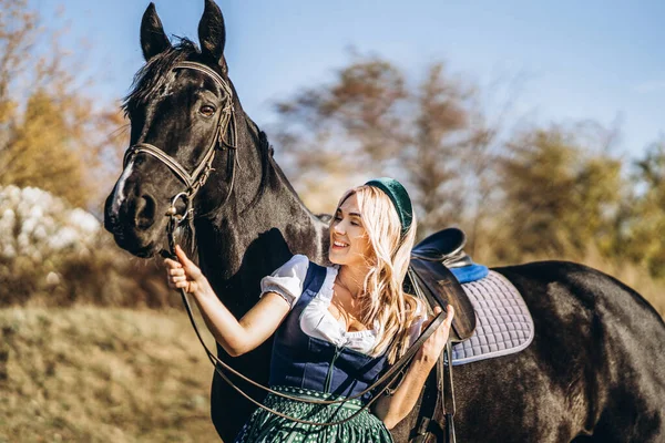 大きな黒い馬を屋外で歩く伝統的なドレスでかなりブロンド 動物と人の友情の概念 — ストック写真