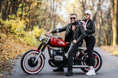 Ormandaki yolda, kırmızı motorsikletin yanında, renkli, mavi arka planda güzel bir çift. İlişki kavramı.