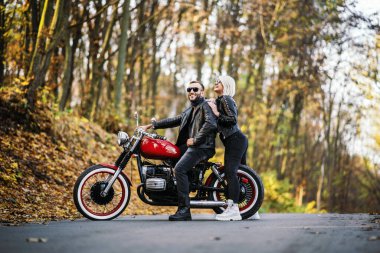 Ormandaki yolda, kırmızı motorsikletin yanında, renkli, mavi arka planda güzel bir çift. İlişki kavramı.