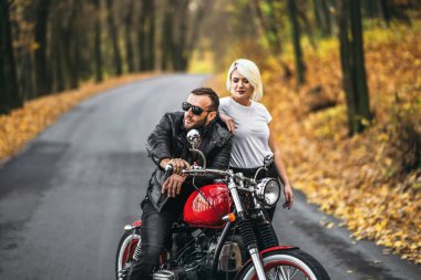 Ormandaki yolda, kırmızı motorsikletin yanında, renkli, mavi arka planda güzel bir çift. İlişki kavramı.