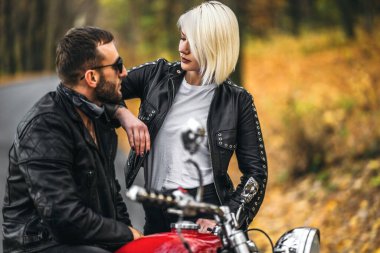 Ormandaki yolda, kırmızı motorsikletin yanında, renkli, mavi arka planda güzel bir çift. İlişki kavramı.