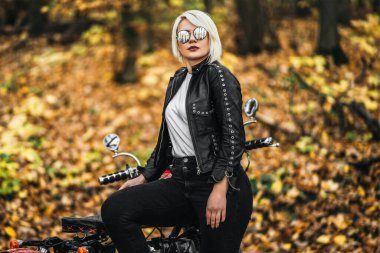 Kırmızı motosikletli, güneş gözlüklü güzel sarışın motosikletli kız. Ormanda yol kenarında. Renkli, bulanık bir geçmişi var..