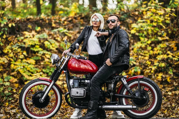 Ormandaki yolda, kırmızı motorsikletin yanında, renkli, mavi arka planda güzel bir çift. İlişki kavramı.