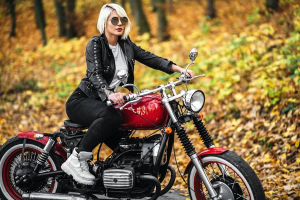 在森林的路上 一个戴着墨镜 戴着红色摩托车 背景五彩斑斓的漂亮金发骑自行车的女孩 — 图库照片