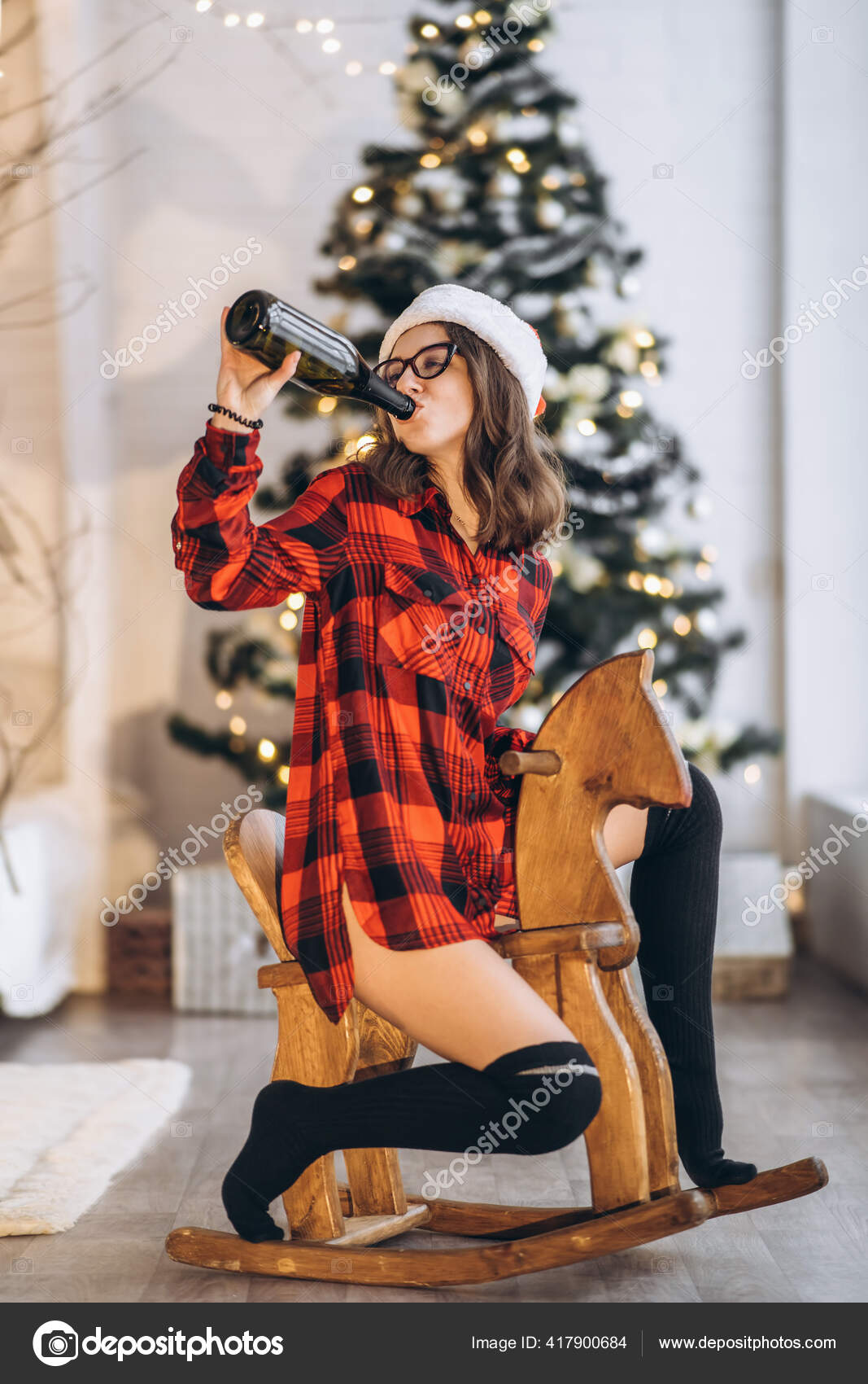 クリスマス シャツや靴下のかわいい女性は シャンパンのボトルと木製のスイング馬のおもちゃに乗って楽しんでいます 新年の木の下に ストック写真 C Bedya クリスマス シャツや靴下のかわいい女性は シャンパンのボトルと木製のスイング馬のおもちゃに乗って楽しんでいます 新年の木の下に ストック写真 C Bedya