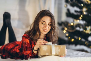 Noel, yeni yıl. Gömlekli ve çoraplı güzel bir kadın Noel hediyesi kutusuyla yatakta yatıyor, yeni yıl ağacı arkasında.