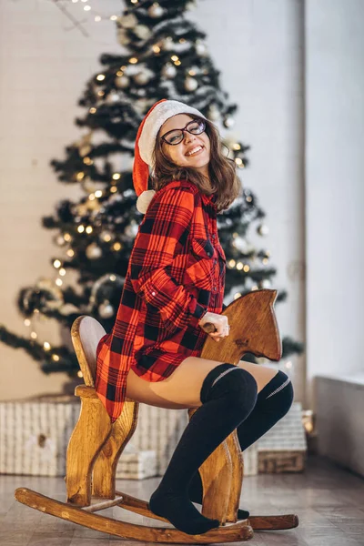 圣诞节 穿着衬衫和袜子的漂亮女人骑在木制的秋马玩具上玩得很开心 — 图库照片