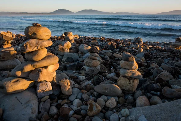 A beautiful seascape with little rock totems erected on the beach. There are mountains at the back