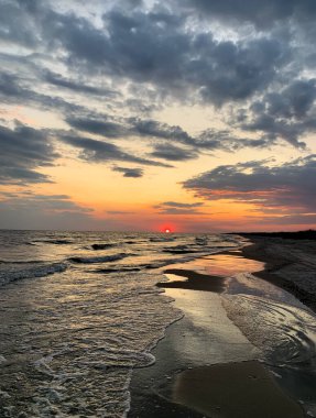 Güzel günbatımının ve köpüklü deniz dalgalarının arka planında kızıl güneş. Sonsuz ufku olan inanılmaz bir sahil manzarası..