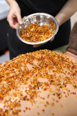 Kaplıca tedavisi doğal Amber. Master elinde amber, küçük taşlarla adamın arka yağmurlama tutar.