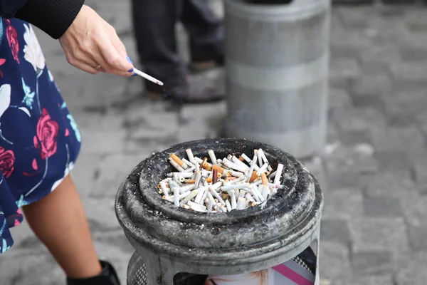 Şehirde bir sürü sigara izmariti olan kül tablasının yanında bir kadının elinde sigara