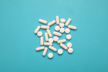 Turkuaz arka planda tıbbi beyaz haplar ve kapsüller