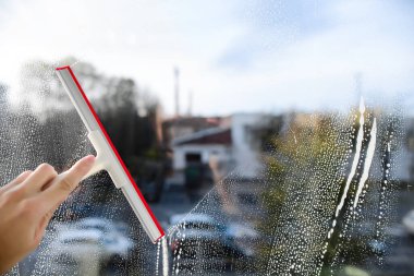 Cam temizleyicisi ve cam sileceği, mavi gökyüzü. Adam elinde bir cam sileceği tutuyor ve penceredeki deterjanı yıkıyor.