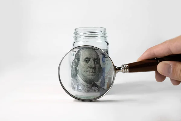 One hundred dollars under a magnifying glass, close-up. The person examines the money in the piggy bank. The concept of increasing income, investing, increasing personal finance