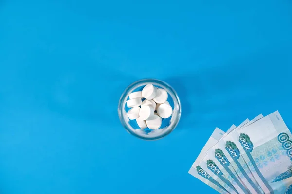 Pills and money on a blue background, top view. Concept of expensive drugs and medicine, payment for treatment, purchase of pills