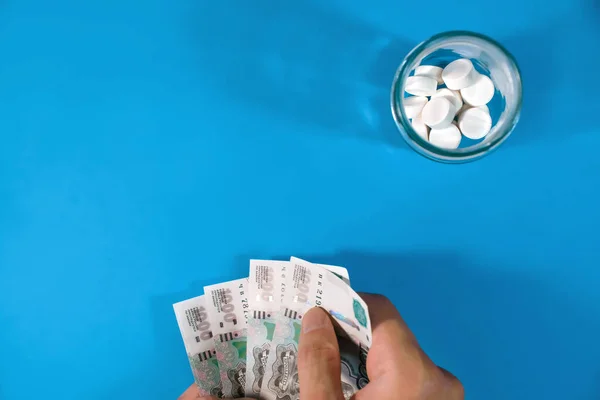 青い背景に丸薬とお金 男は薬の瓶の近くで手に金を持っている 高価な薬や薬の概念 治療費 ワクチンの購入 — ストック写真