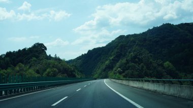 Dağlar aralarından geçen bir yola bakıyor.