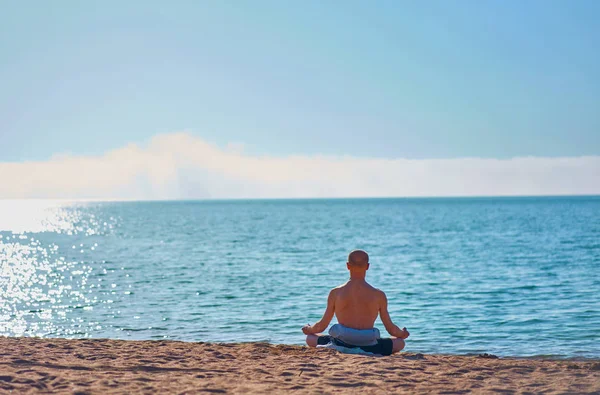 Yaşlı bir adam kumlu sahil manzarasında meditasyon yapıyor.