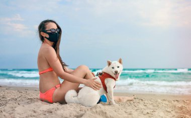 Plajda maskeli bir kız ve bir köpek.