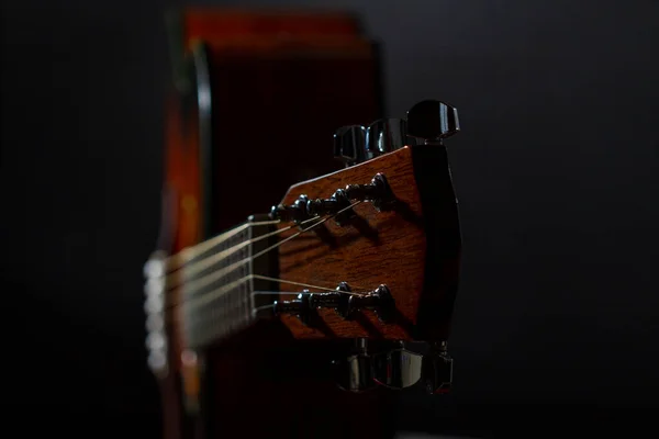 Guitar. Neck head, splitting and fingerboard of an acoustic six-string guitar against a black background.