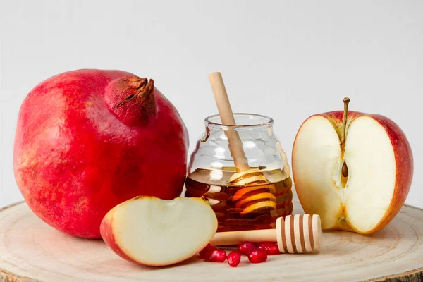 Pomegranate, apple and honey on a light background, the traditional food of the celebration of the Jewish New Year, Rosh Hashanah.