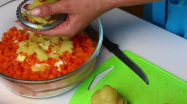 Rus et salatası sebze ve mayonez. Bir kadın haşlanmış patates kesiyor.