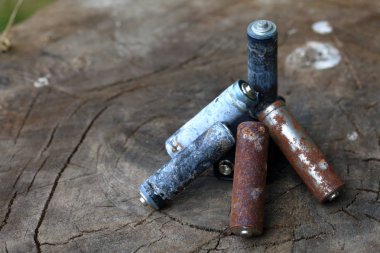 Kullanılmış piller, korozyon ile kaplı. Farklı şekil ve boyutlarda. ahşap kütük kenarında yalan. Çevre koruma, geri dönüşüm.