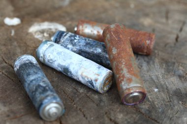 Kullanılmış piller, korozyon ile kaplı. Farklı şekil ve boyutlarda. ahşap kütük kenarında yalan. Çevre koruma, geri dönüşüm.