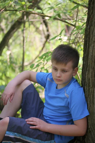 Bir gencin parkta yürürken bir fotoğrafçı için poz veriyor. Oturur, ağaca yaslanmış.