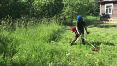 Bir adam bir benzin örgü ile çalışıyor. Oblique yan yana önde gelen tarama alanı, yatıyor. Koruyucu net yükseltir ve çim inceler.