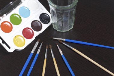 Suluboya ve karanlık bir yüzey üzerinde fırçalar. Yakınlarda Su için bir camdır. Yaratıcılık için konular.