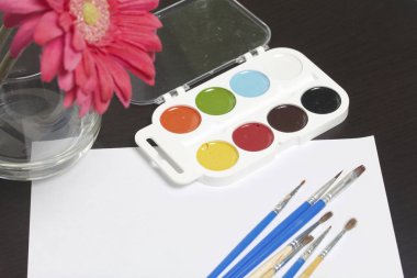 Suluboya ve karanlık bir yüzey üzerinde fırçalar. Yakınlarda bir vazoda natürmort için yapay bir çiçektir. Yaratıcılık için konular.