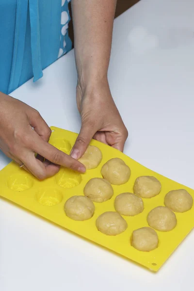 On the table lie pieces of dough in the form of balls. The woman fills them with a silicone baking dish.