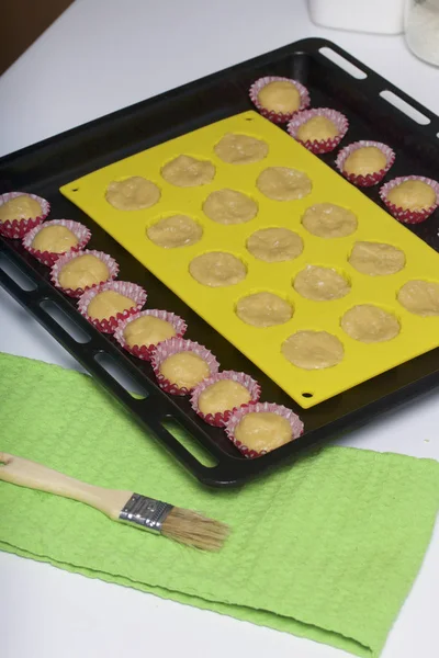 On the baking sheet is a silicone mold with a dough. Also small paper forms filled with dough.