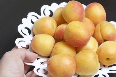 Bir adam bir yemek meyve alır. Kayısı ile bir yemek bir karanlık tablo üstünde duruyor.