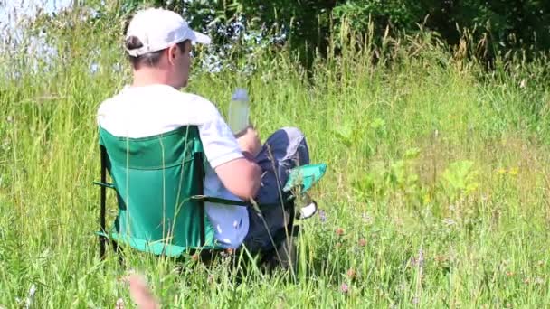 Hombre Sienta Una Silla Picnic Prado Iluminado Descansando Bebiendo Agua — Vídeos de Stock