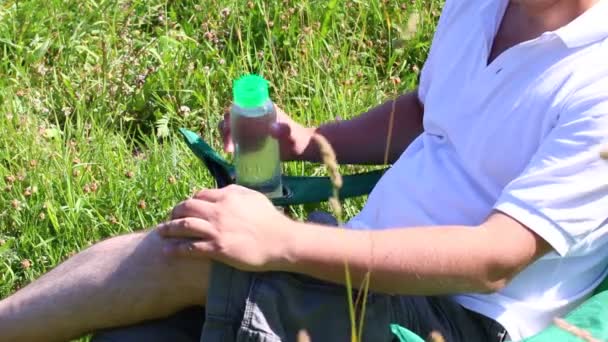 Man Sits Picnic Chair Lighted Meadow Rests Opens Bottle Water — Stock Video