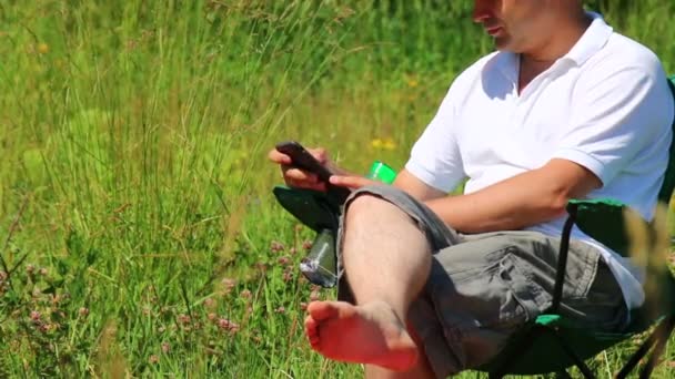 Homem Senta Uma Cadeira Piquenique Dobrável Joga Smartphone — Vídeo de Stock