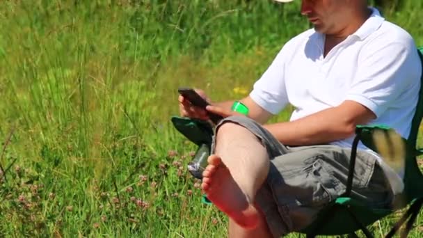 Homem Senta Uma Cadeira Piquenique Dobrável Joga Smartphone Depois Levanta — Vídeo de Stock