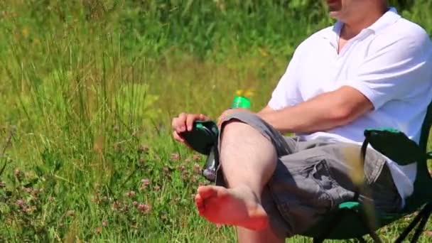 Bir Adam Bir Katlanır Piknik Sandalyede Oturur Suyu Içer — Stok video